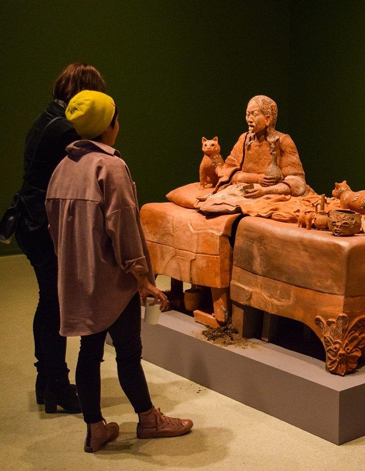 two students view a clay sculpture of a woman and cat